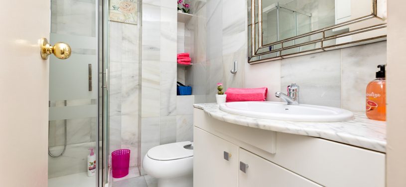 Baño con plato de ducha y mampara, tonos blancos, gran espejo en el lavabo