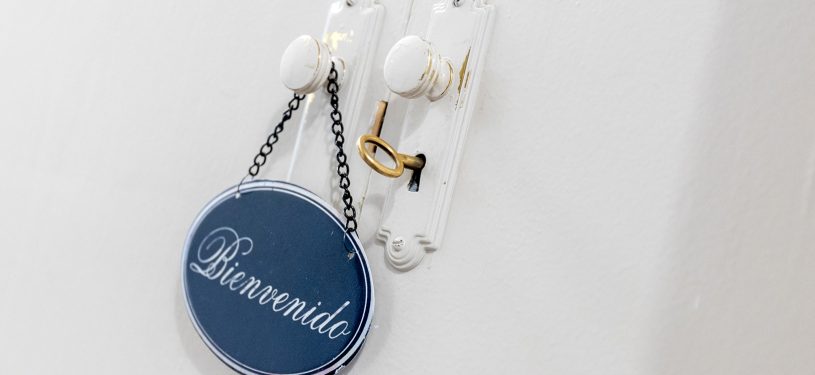 Pomo de puerta con un cartel de bienvenida en azul, con la llave de color madera introducida en la cerradura